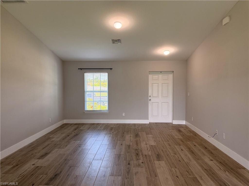 Spacious room featuring wood-finish flooring, neutral-toned walls, and bright overhead lighting