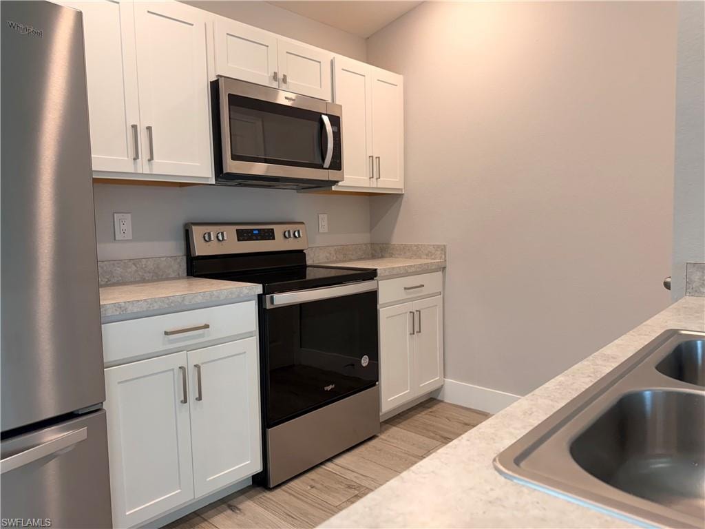 Kitchen featuring white shaker cabinetry, stainless steel appliances, light-toned countertops, and wood-finish flooring