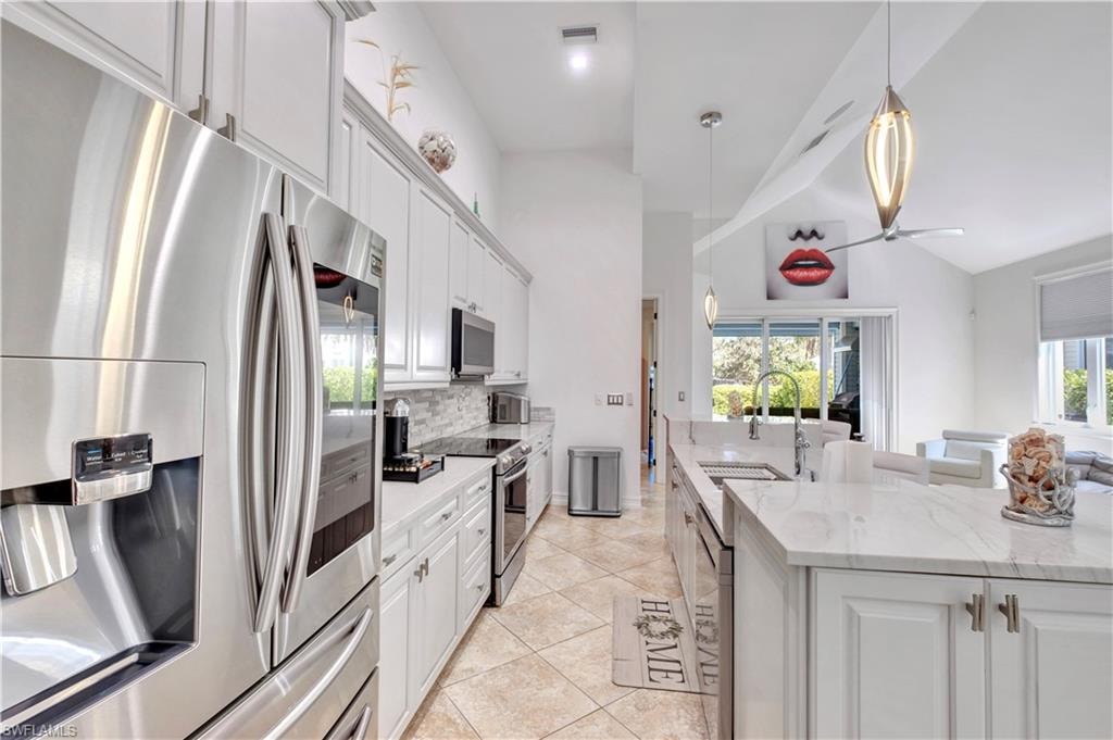 Stainless steel appliances with a side-by-side refrigerator, white shaker cabinetry, tiled backsplash, and light-toned countertops