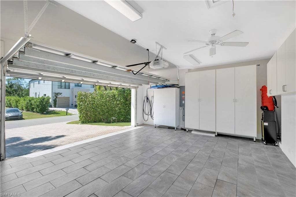Spacious garage featuring wood-finish tile flooring, extensive built-in cabinetry, ceiling fan, and overhead lighting