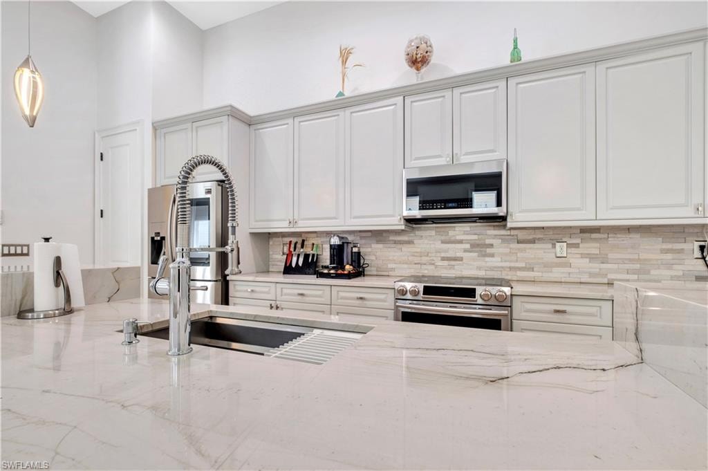 Kitchen island featuring a stainless steel sink with a high-arc faucet, light-toned countertops, and light gray cabinetry