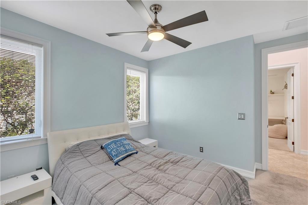 Bedroom featuring a ceiling fan with integrated lighting, two windows with blinds, and light blue walls