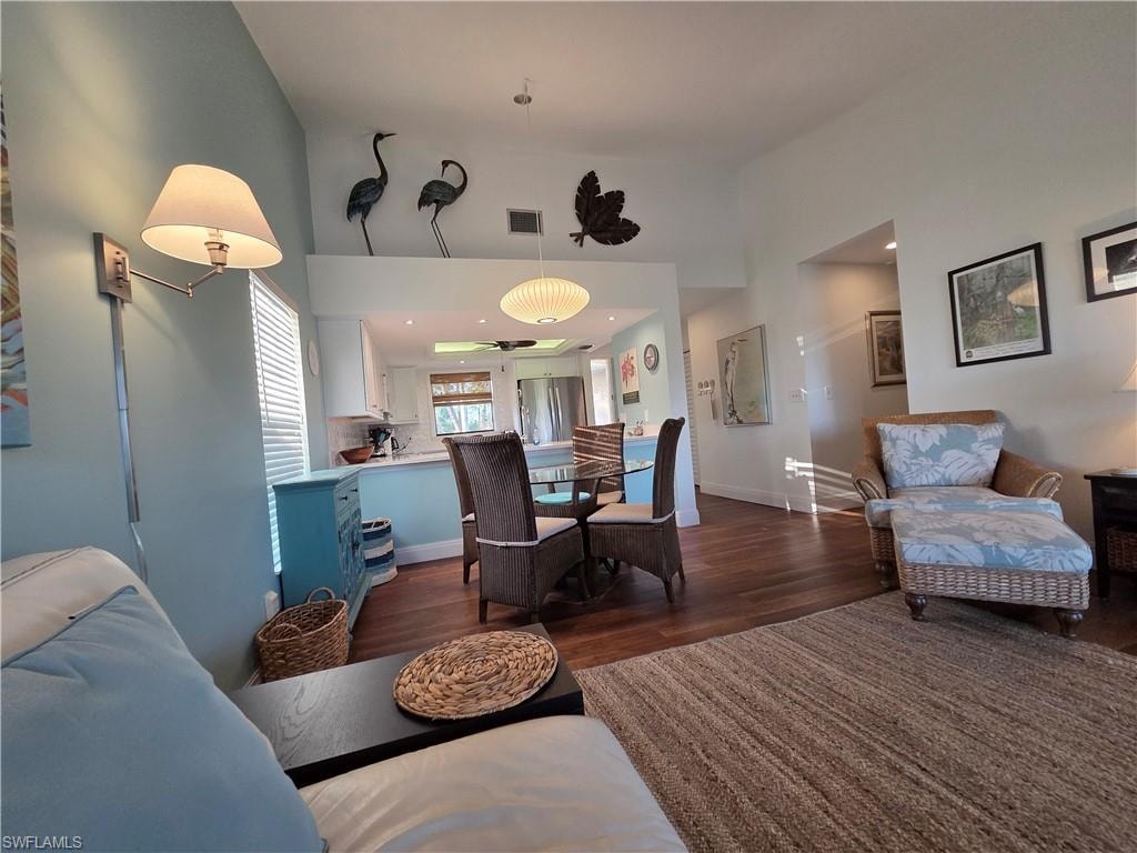 This property features a bright living area with vaulted ceilings and hardwood flooring, a dining area with a glass-top table, and a kitchen with white cabinetry and light blue lower cabinets