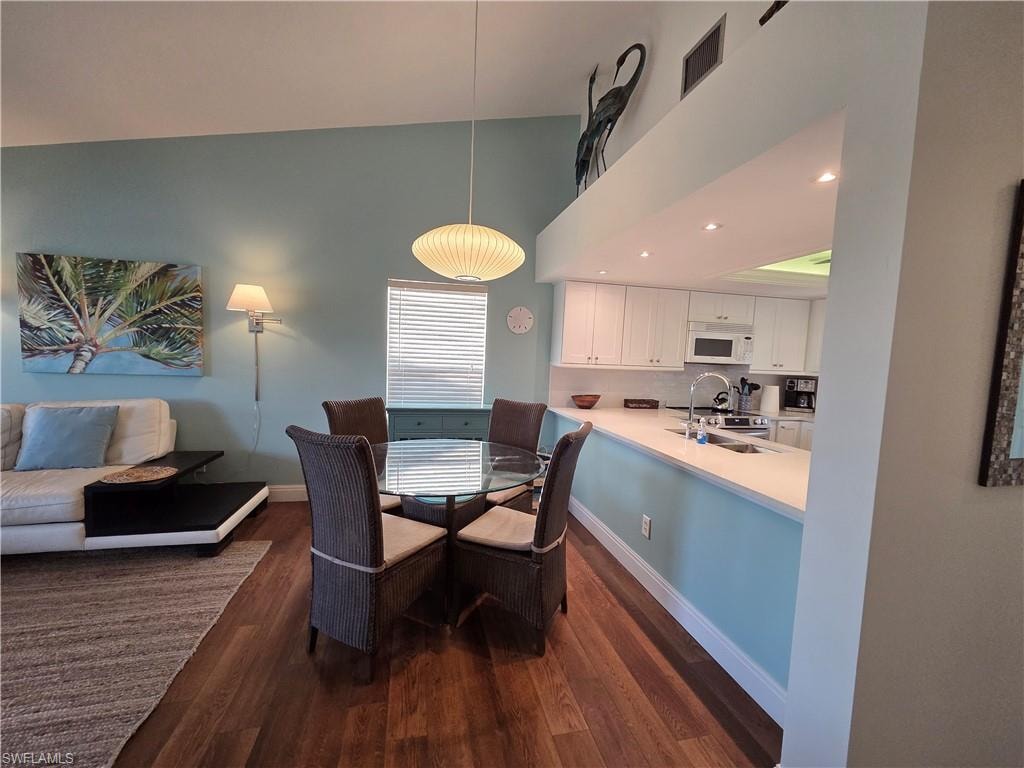 Open concept living space featuring wood flooring, a dining area with a glass-top table, and a kitchen with white cabinetry and a breakfast bar