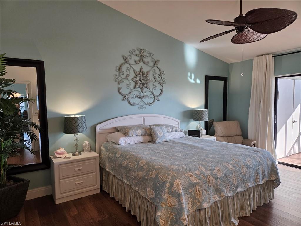 Vaulted ceiling bedroom featuring wood-finish flooring, a white paneled headboard, and a dark woven ceiling fan