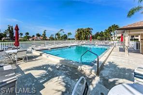 Community swimming pool with a concrete sundeck, white picket fencing, and palm trees