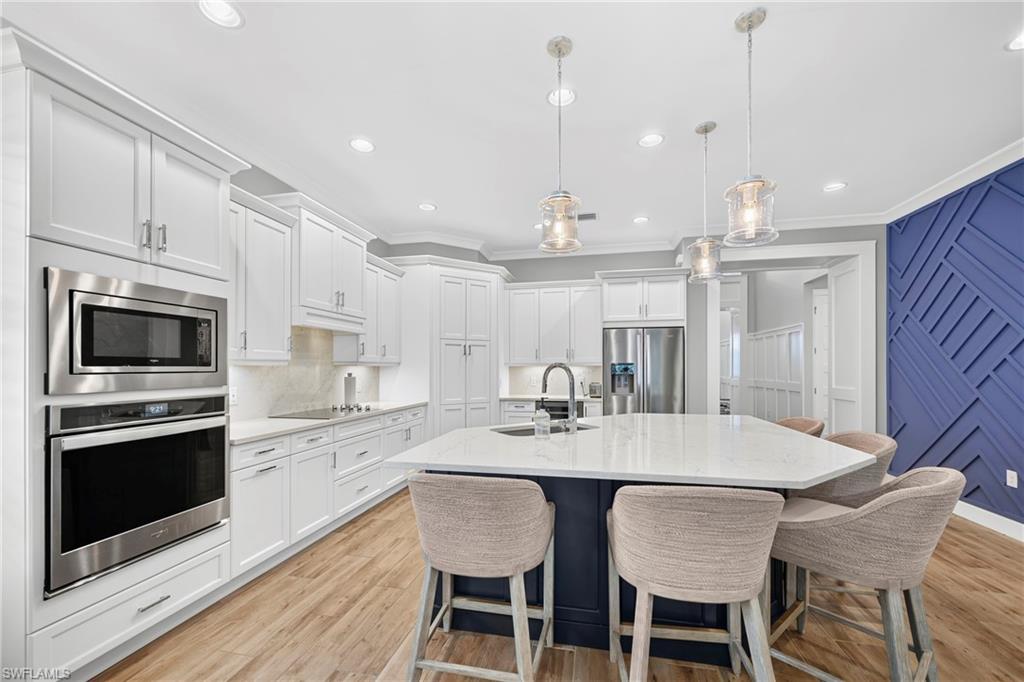 Open-concept kitchen featuring an oversized island with seating, extensive white cabinetry, built-in stainless steel appliances, pendant lighting, and wood-finish flooring