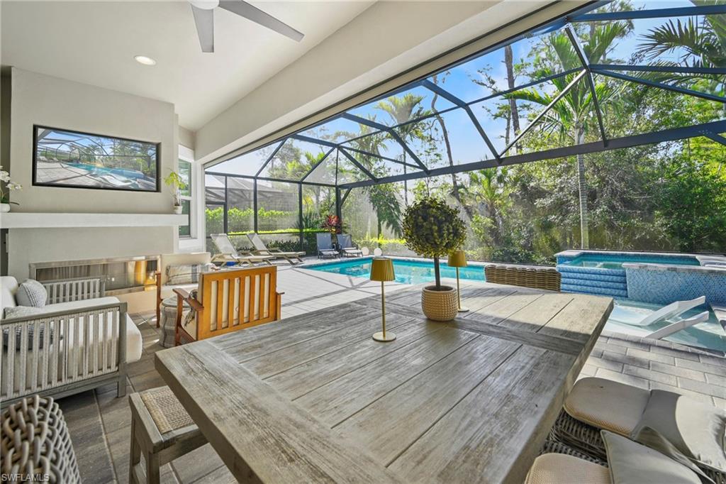 Screened lanai featuring a swimming pool, integrated spa with mosaic tile detailing, and a spacious dining area with a wood-finish table