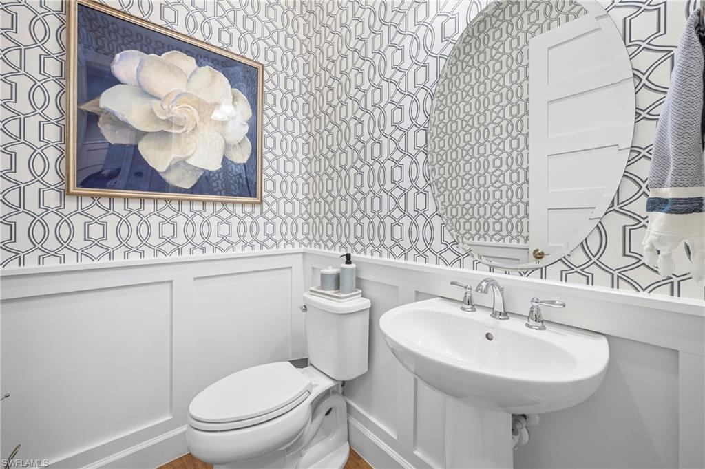 Pedestal sink with chrome faucet hardware, set against a geometric pattern wallpaper and white wainscoting