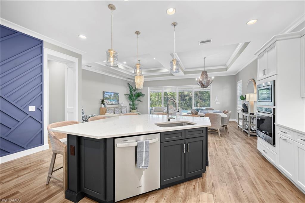 Gourmet kitchen featuring a large island with sink, stainless steel appliances, abundant cabinetry, wood-finish flooring, and a coffered ceiling