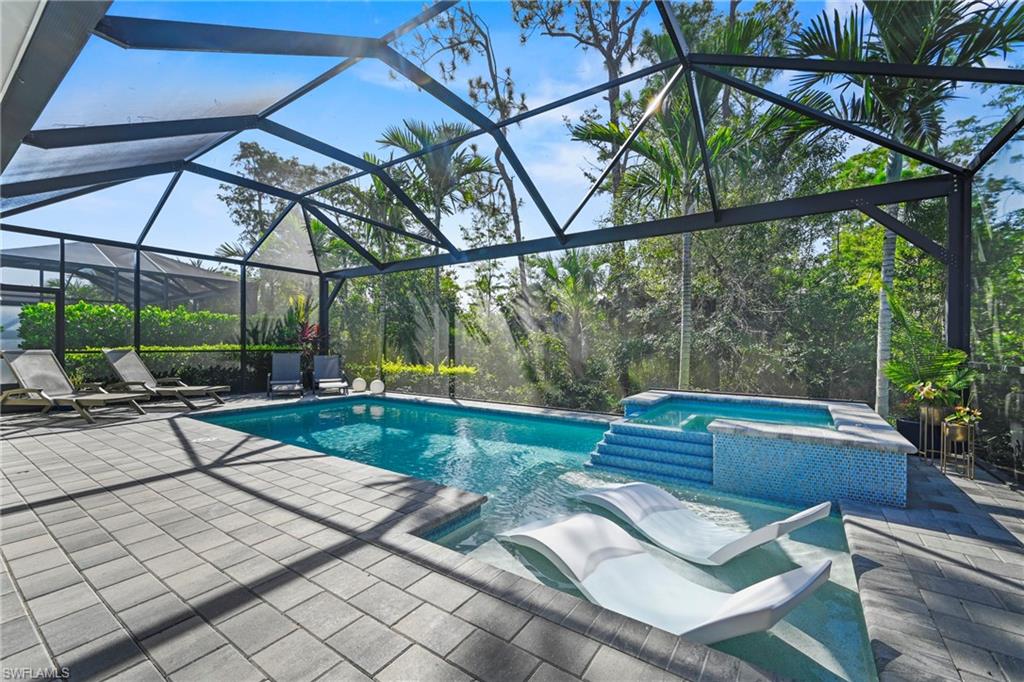 Screen-enclosed pool deck featuring a swimming pool with integrated spa, sun shelf, and paver surfacing