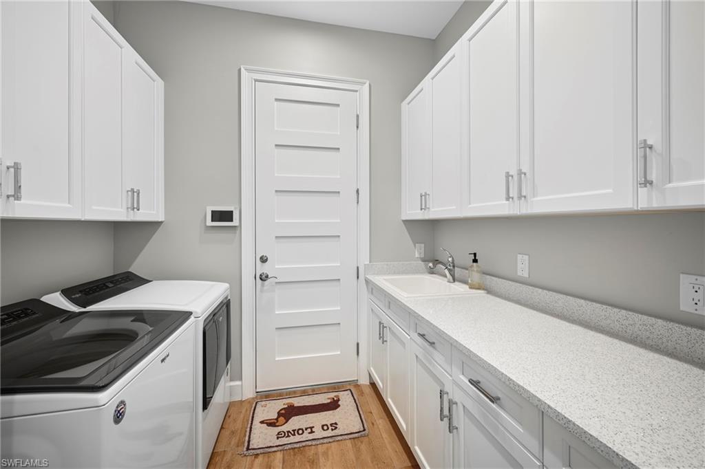 Laundry room featuring extensive white cabinetry, light-toned countertops, a utility sink, and wood-finish flooring
