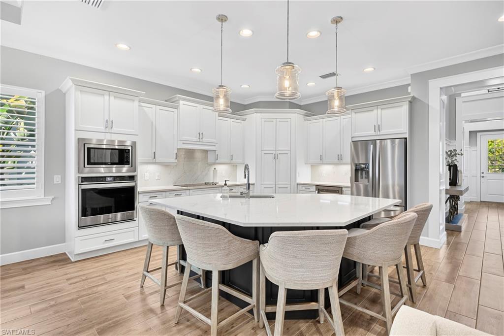 Modern kitchen featuring a large multi-sided island with seating, white shaker cabinetry, stainless steel appliances, and wood-finish flooring