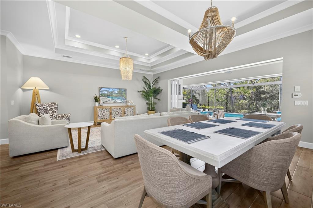Spacious indoor-outdoor living area featuring wood-finish flooring, a tray ceiling with recessed lighting, and a large sliding glass door opening to a screened lanai with a pool
