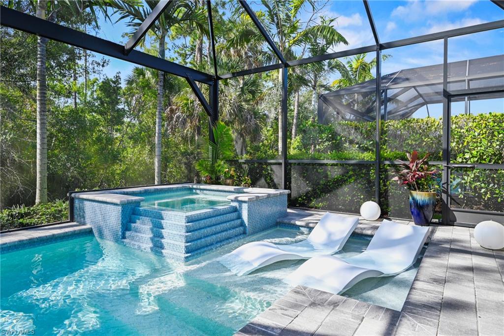 Screened outdoor living area featuring a pool with an integrated spa, mosaic tile accents, and an adjacent paver patio
