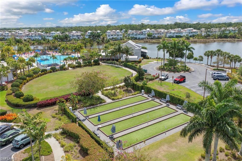 Expansive community green space featuring multiple bocce ball courts, a large swimming pool area, manicured lawns, mature palm trees, and waterfront access