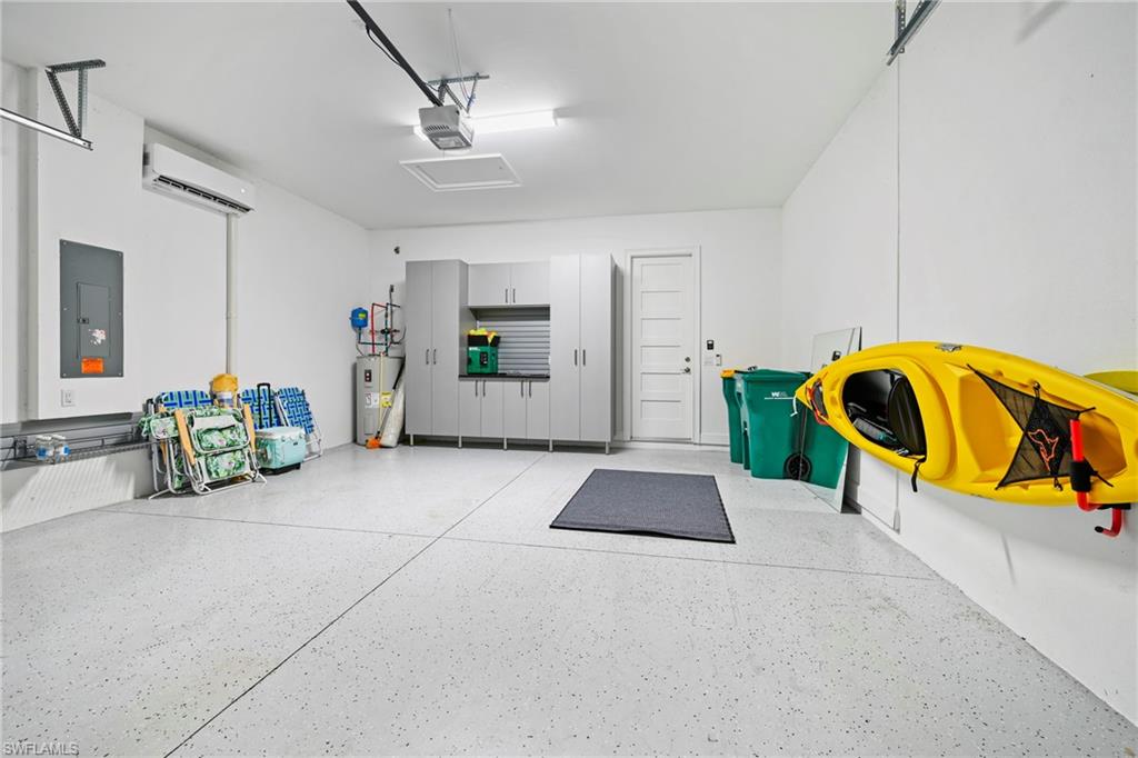 Spacious garage featuring epoxy flooring, built-in cabinetry, mini-split air conditioning unit, water heater, and a paneled interior door