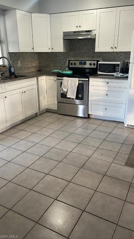 Kitchen featuring white shaker-style cabinetry, a stainless steel range with overhead hood, and a stone-finish backsplash