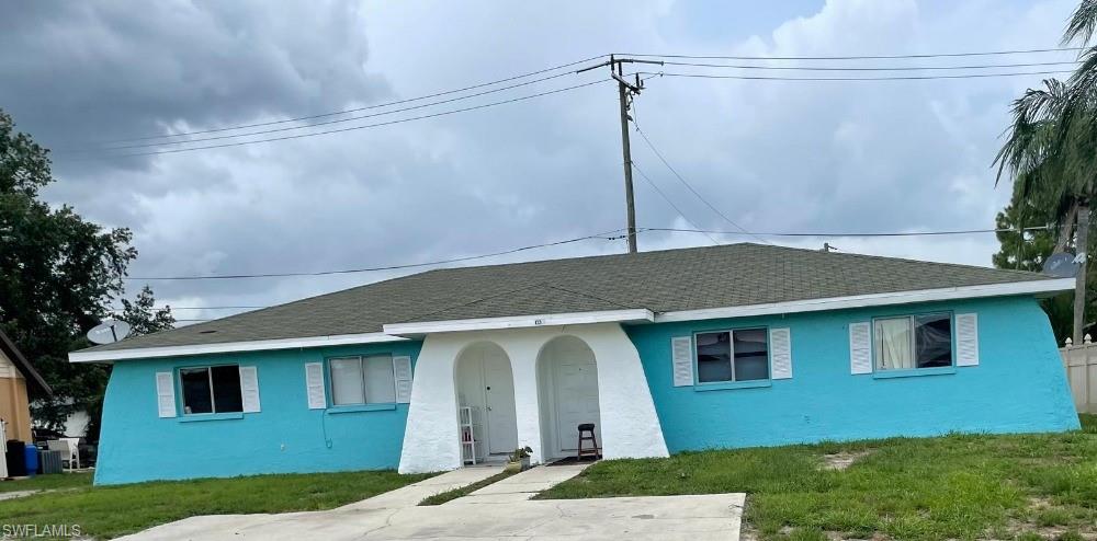 Duplex property with a teal exterior finish, white arched entryway, white window shutters, a dark shingle roof, and a concrete driveway