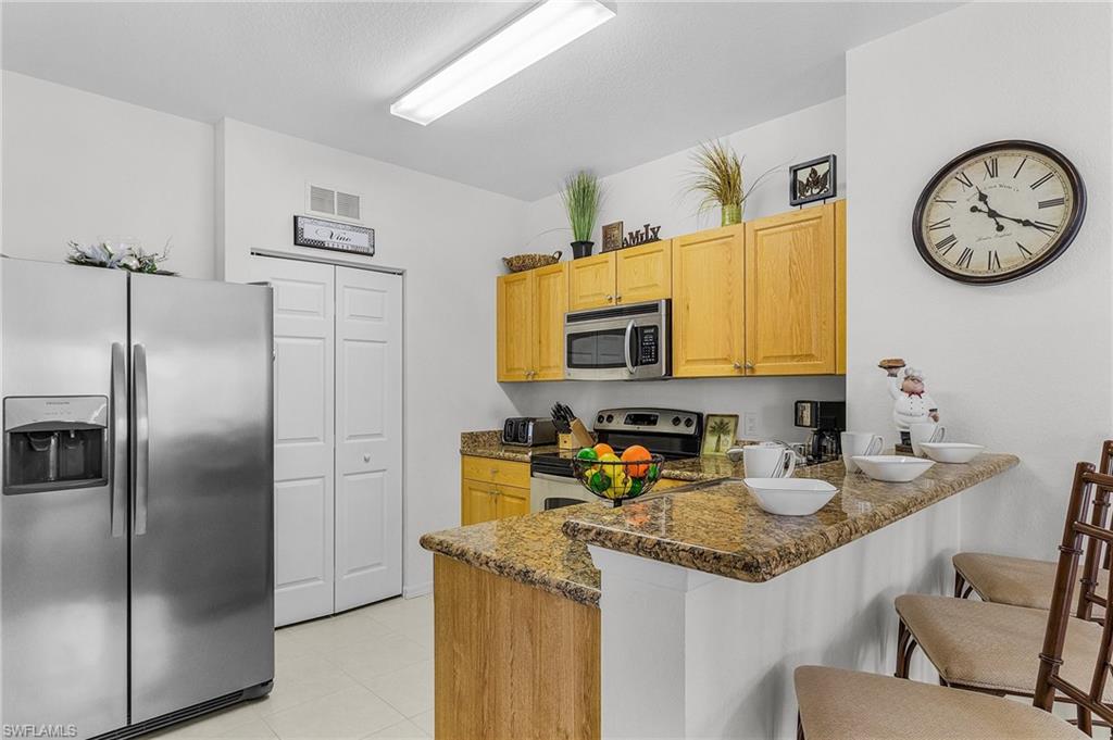 Kitchen with stainless steel appliances, a peninsula, a breakfast bar, dark stone countertops, and light brown cabinetry