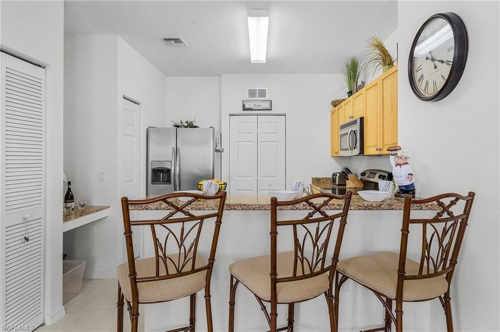 Kitchen with a breakfast bar, appliances with stainless steel finishes, light brown cabinets, light tile patterned flooring, and a peninsula