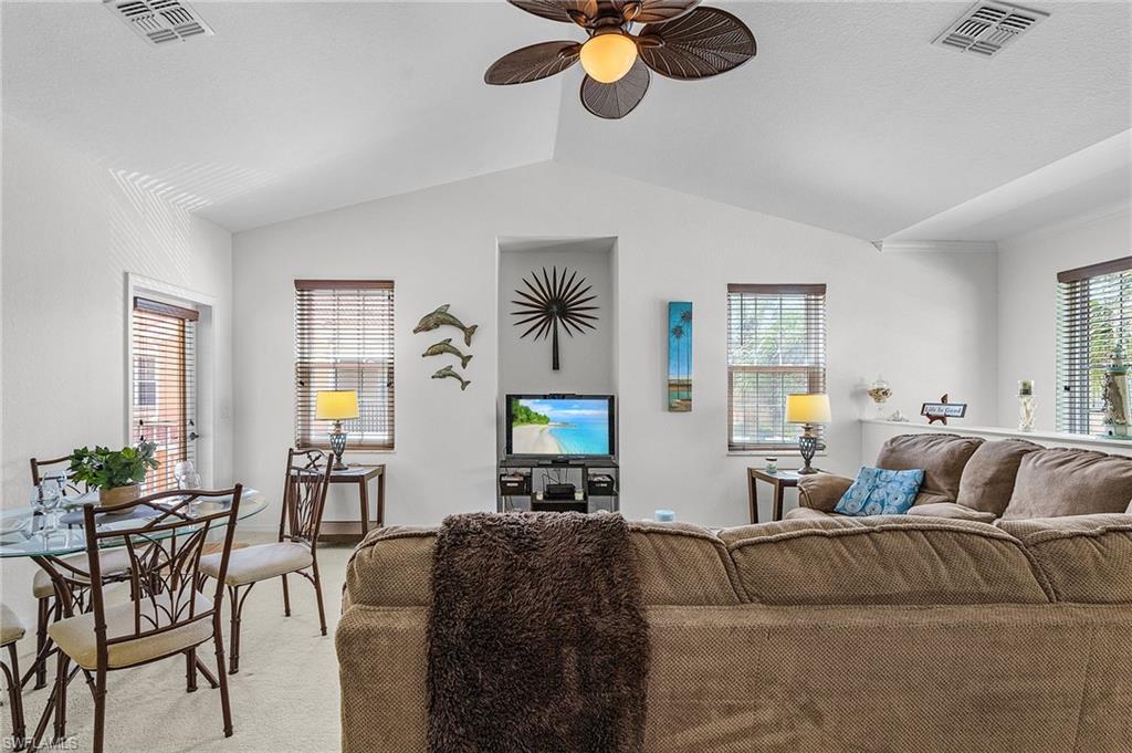 Carpeted living room with lofted ceiling, healthy amount of natural light, and a ceiling fan