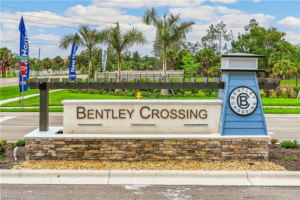Community entrance sign for Bentley Crossing featuring stacked stone base, light-colored signage, blue-paneled architectural element, dark-toned pergola, and surrounding landscaping