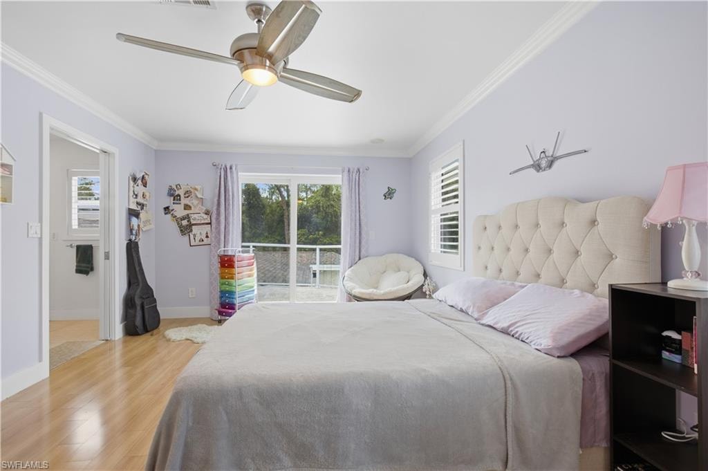 Bedroom featuring wood-finish flooring, a ceiling fan with integrated lighting, a sliding glass door with balcony access, and a window with plantation shutters