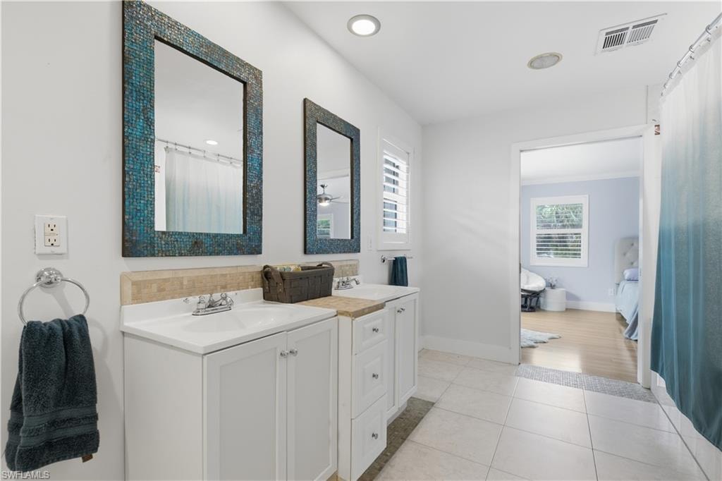 Double vanity bathroom featuring white cabinetry and countertops, individual sinks, and decorative framed mirrors