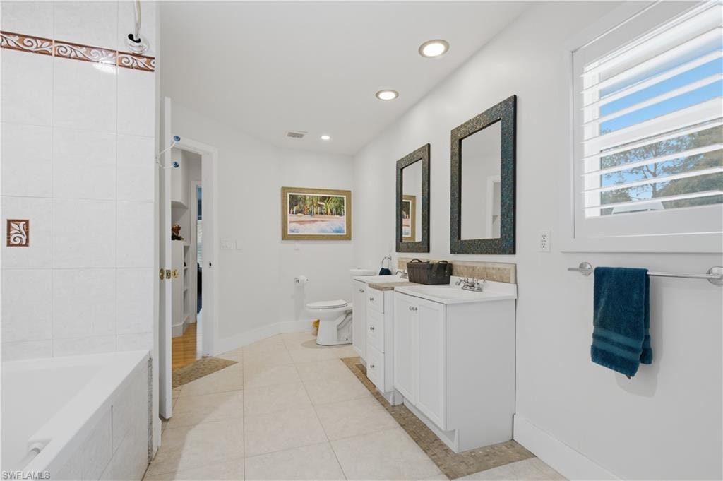 Bathroom featuring a built-in tub with tile surround, dual vanity with undermount sinks, and a window with plantation shutters