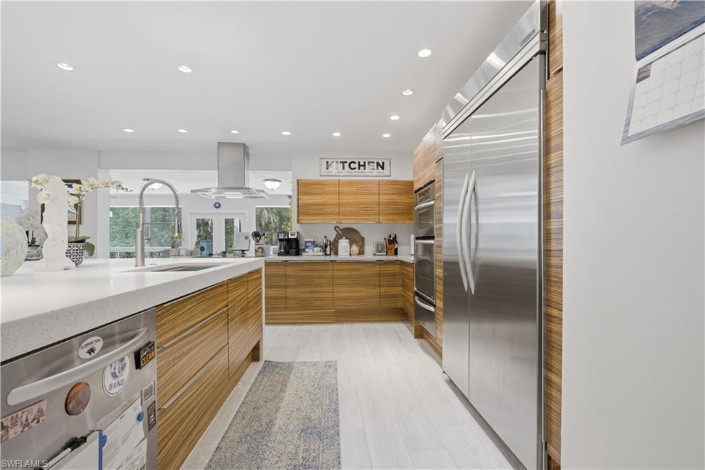 Modern kitchen featuring light wood-finish cabinetry, stainless steel appliances, a large center island with an undermount sink, and recessed lighting