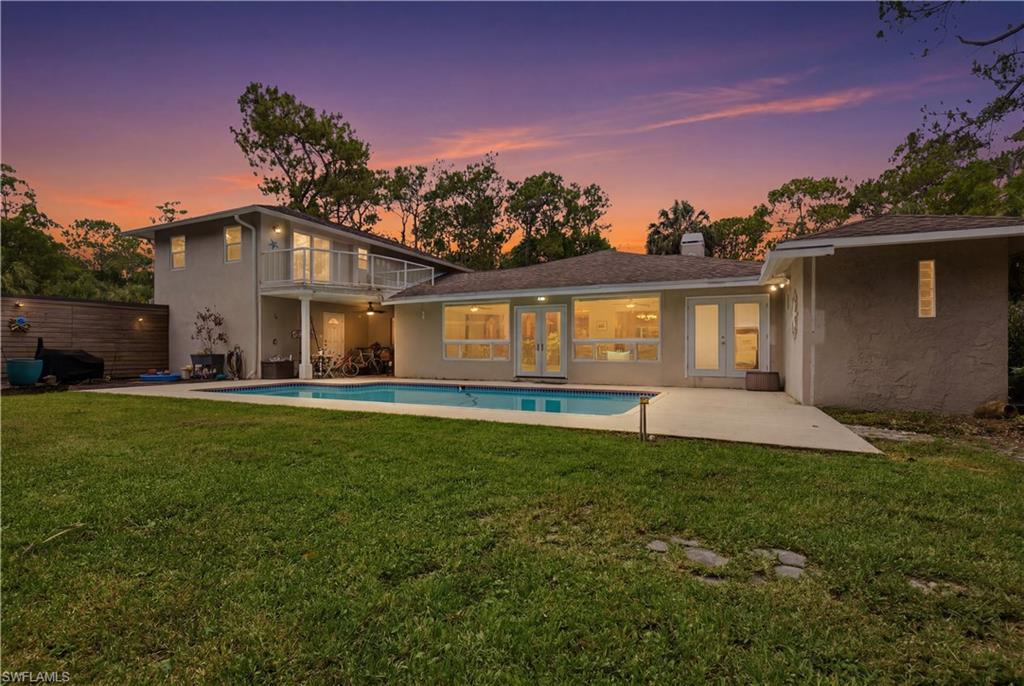 Expansive backyard featuring a large in-ground swimming pool, concrete patio, a private second-story balcony with white railing, and a ground-floor covered patio