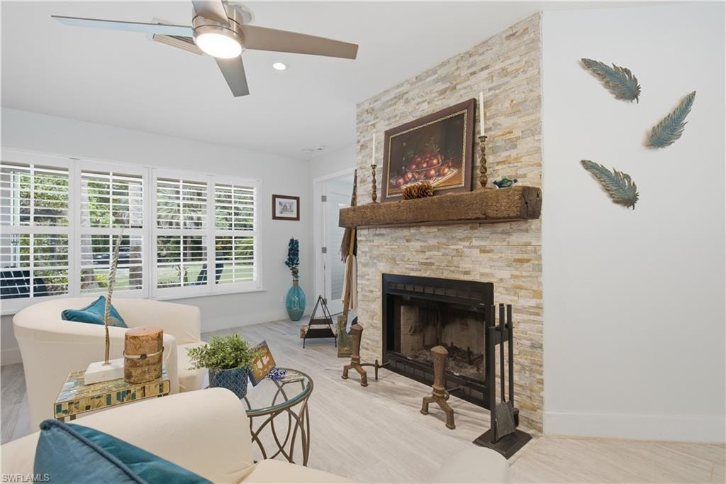 Living area featuring a stone-clad fireplace with a substantial timber mantelpiece, light wood-finish flooring, white plantation shutters, a ceiling fan with integrated lighting, and recessed lighting