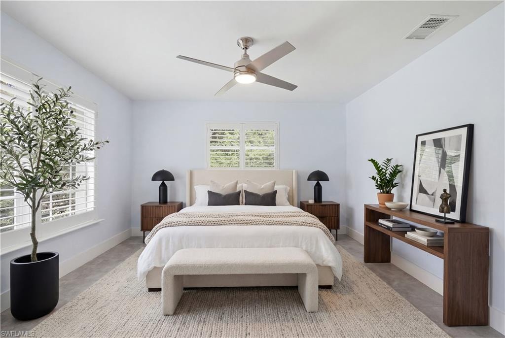 Spacious bedroom featuring light-toned walls, two windows with plantation shutters, a ceiling fan with integrated lighting, and light gray tile flooring