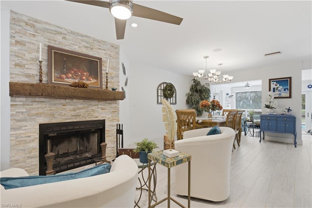 Living area featuring a stacked stone fireplace with a substantial wood mantel, a ceiling fan, and light wood-finish flooring extending into the dining space