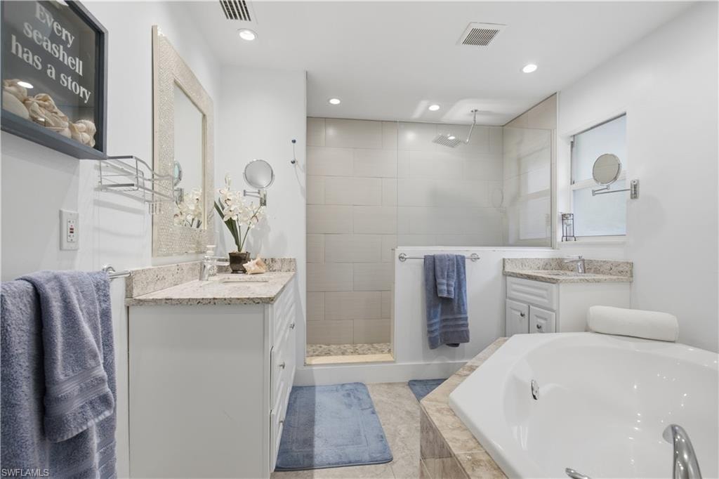 Spacious bathroom featuring a built-in jetted tub, a walk-in shower with a rain showerhead, a dual vanity with stone countertops, and recessed lighting