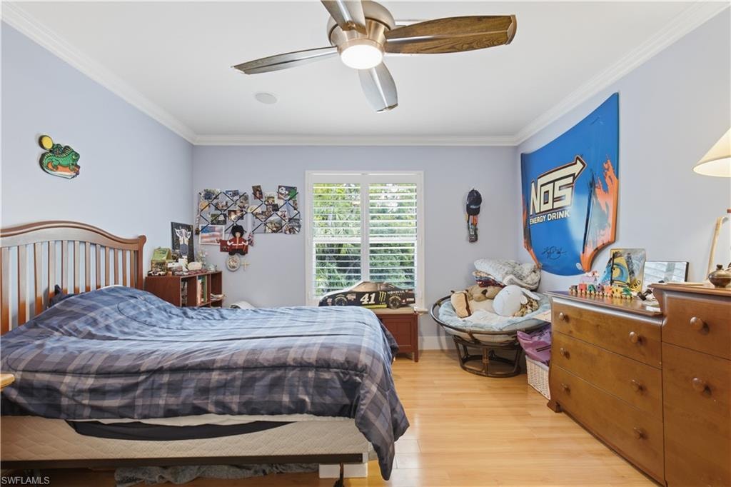 Bedroom featuring wood-finish flooring, a ceiling fan with light fixture, plantation shutters, and crown molding