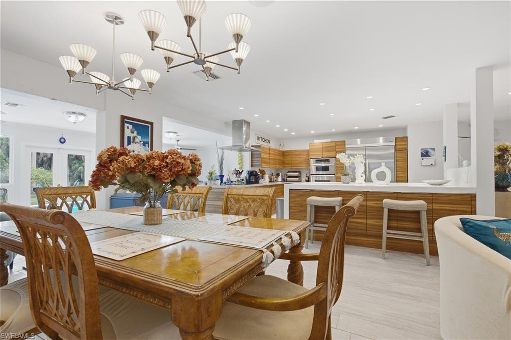 Spacious dining area featuring two contemporary multi-arm chandeliers, wood-finish flooring, and a dining table with six carved wood chairs