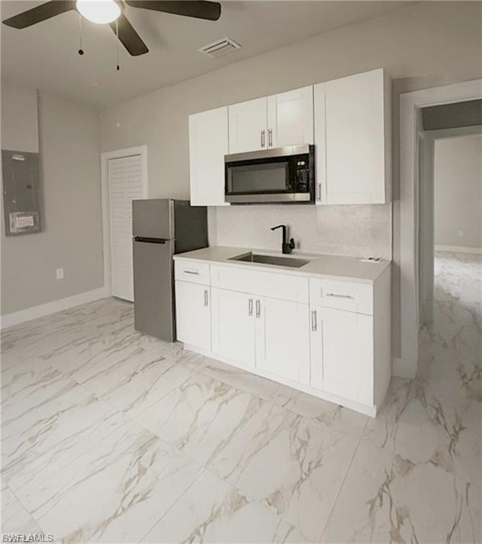 Kitchenette featuring white cabinetry, stainless steel microwave, stainless steel refrigerator, black faucet, and stone-look tile flooring