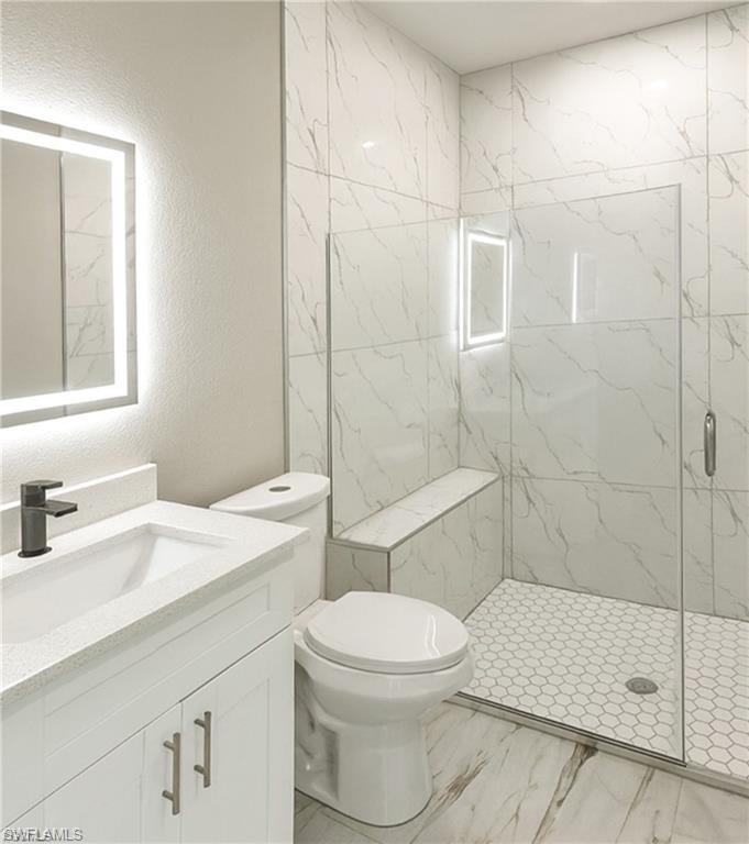 Modern bathroom featuring an illuminated vanity mirror, a single-sink vanity with a light-colored countertop, and a glass-enclosed shower