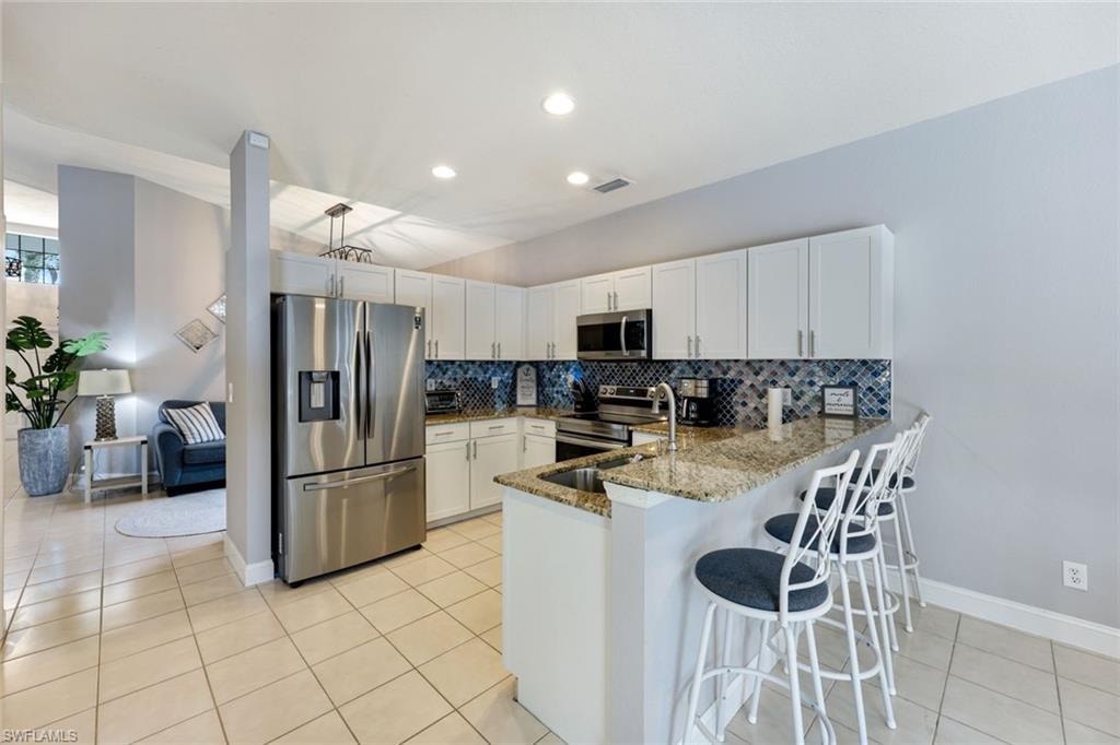 Kitchen featuring stainless steel appliances, a peninsula, tasteful backsplash, stone countertops, and light tile patterned floors