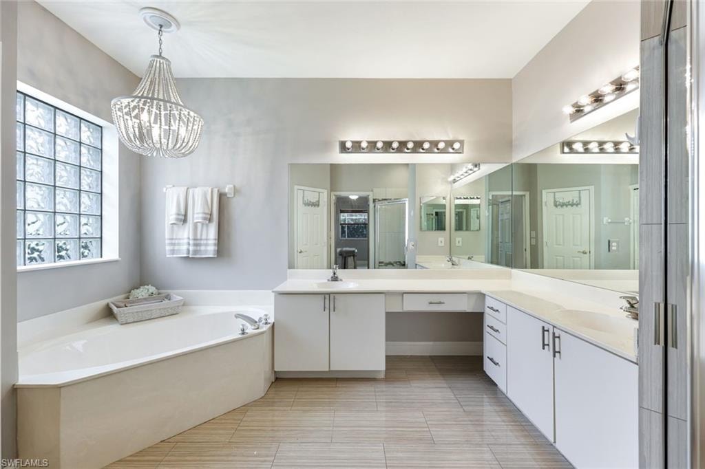 Full bath featuring a garden tub, double vanity, a stall shower, and a chandelier