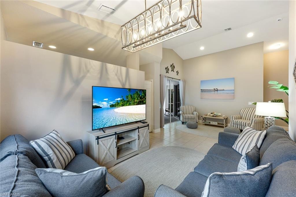 Living area with light tile patterned floors, recessed lighting, a chandelier, and a towering ceiling