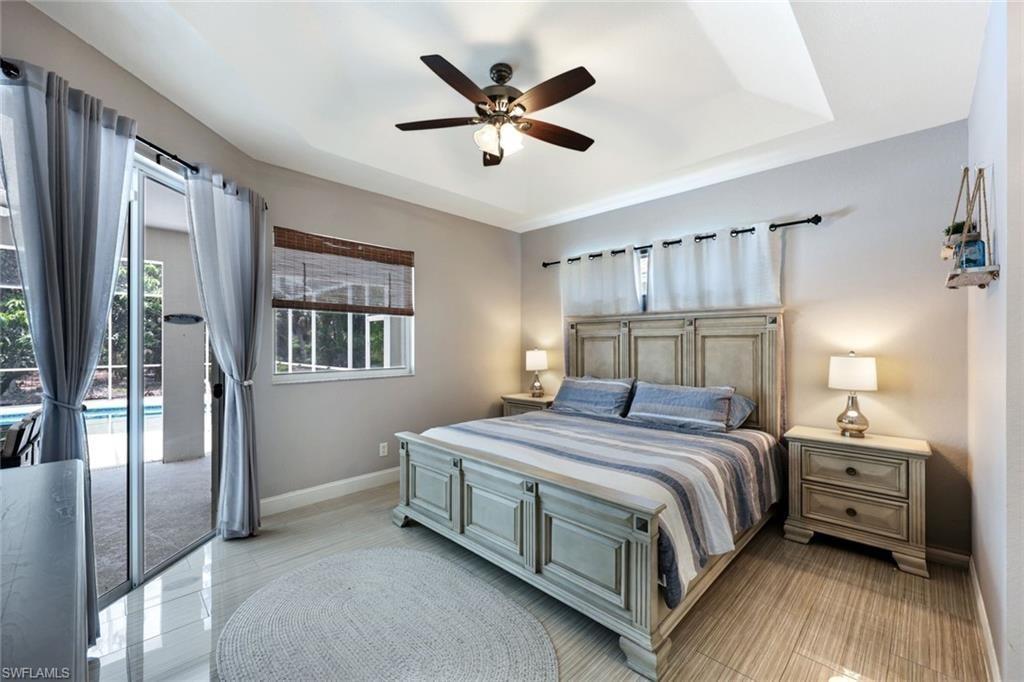 Bedroom with access to exterior, a tray ceiling, and a ceiling fan