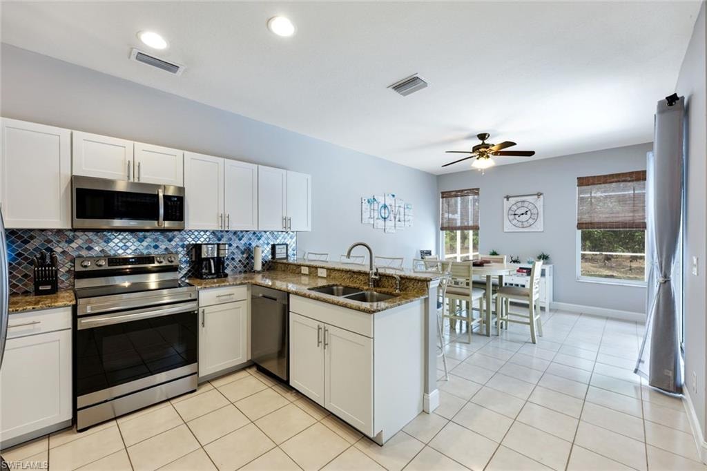 Kitchen with appliances with stainless steel finishes, a peninsula, decorative backsplash, ceiling fan, and white cabinetry