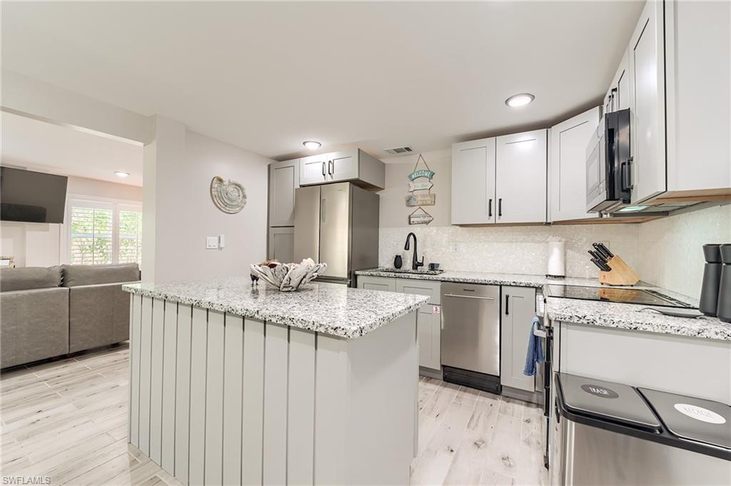 1st Floor Kitchen with a kitchen island, light stone countertops, tasteful backsplash, stainless steel appliances, and open floor plan- Virtually Edited Image