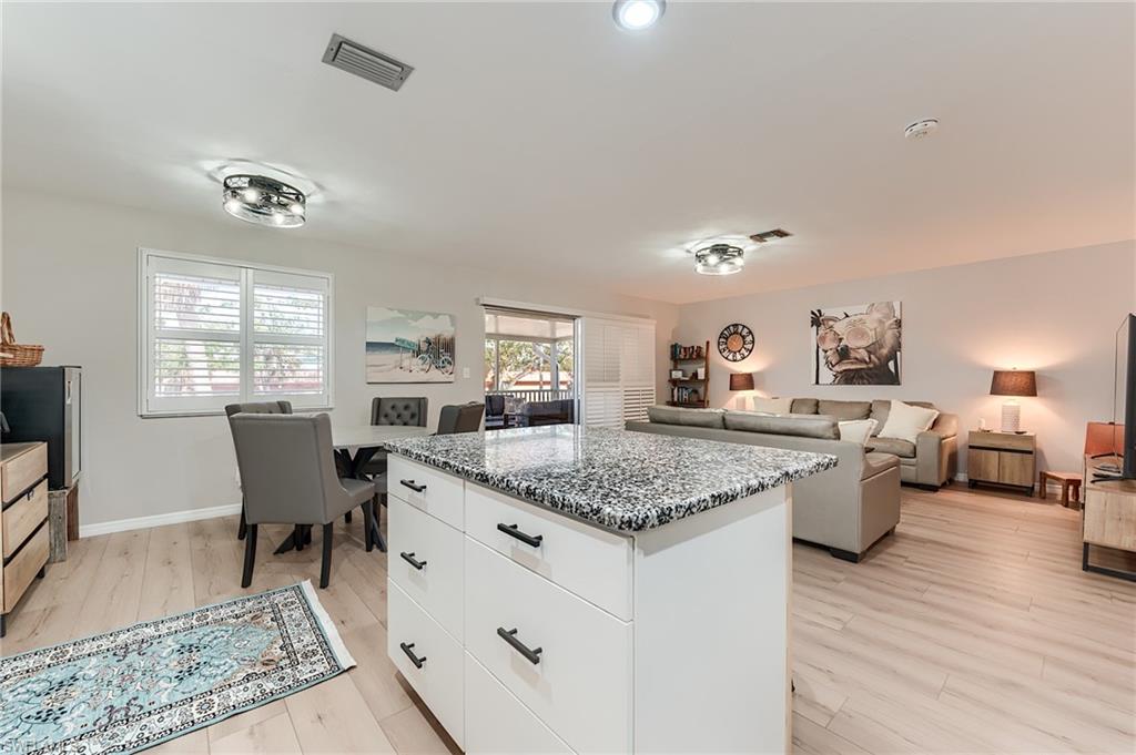 2nd Level Kitchen with a kitchen island, open floor plan, dark stone counters, white cabinetry, and light wood-type flooring- Virtually Edited Image