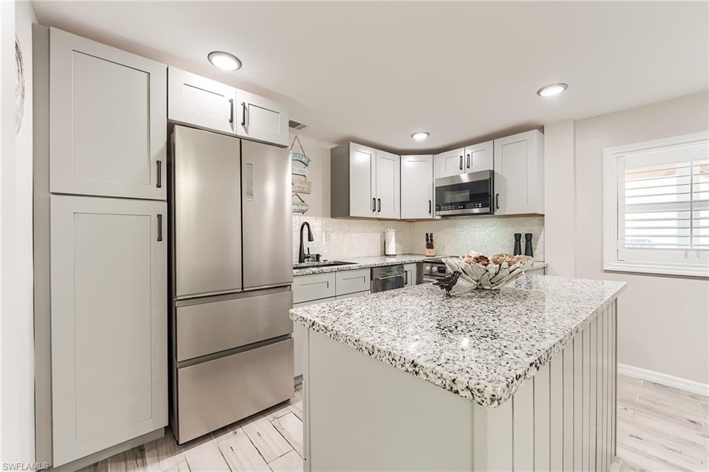 1st Floor Kitchen featuring stainless steel appliances, light stone counters, a center island, tasteful backsplash, and light wood-style flooring- Virtually Edited Image