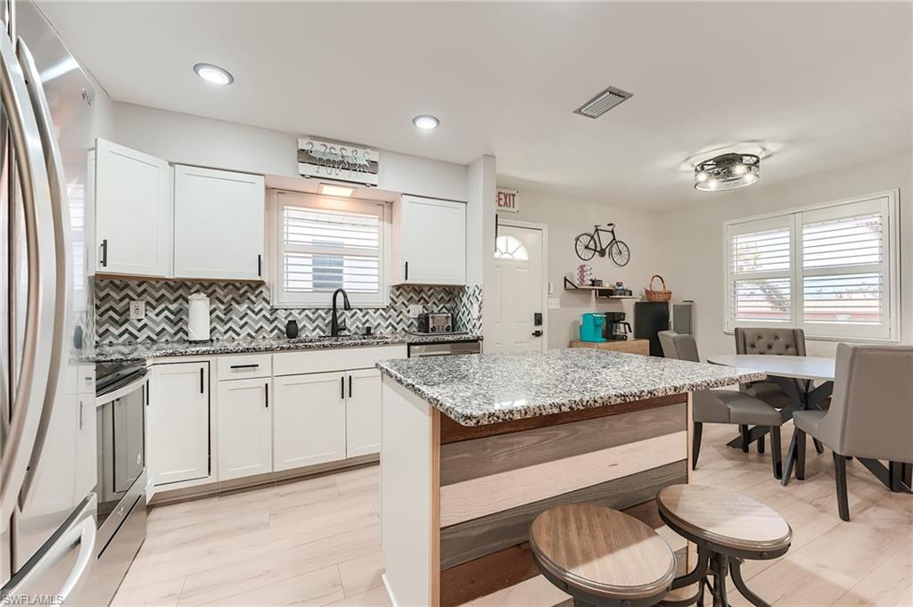2nd Level Kitchen with light stone countertops, decorative backsplash, appliances with stainless steel finishes, white cabinetry, and a kitchen island- Virtually Edited Image