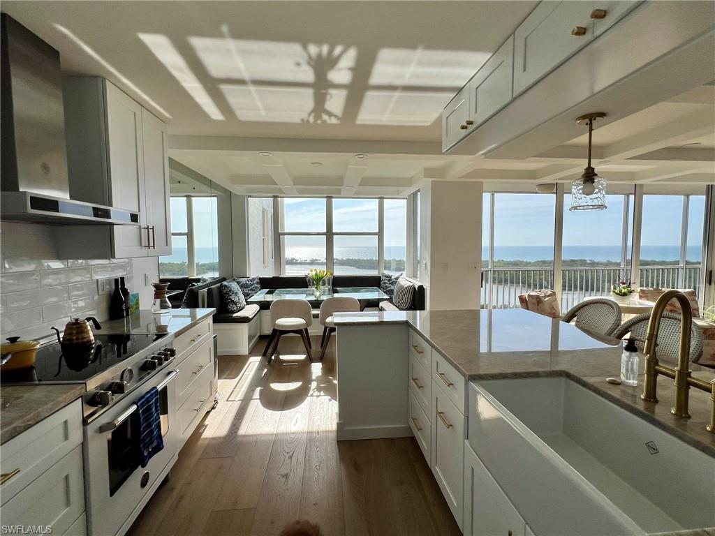 Gourmet kitchen featuring a stainless steel range hood, white subway tile backsplash, light wood-finish flooring, and white cabinetry with brass hardware